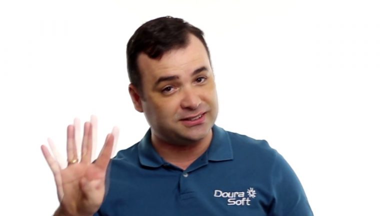 Um homem vestindo uma camisa polo azul da Doura Soft, sorrindo e levantando quatro dedos, está sobre um fundo branco simples - perfeito para ilustrar uma cobrança diária eficiente.