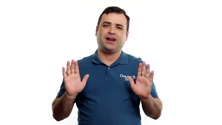 Um homem vestindo uma camisa polo azul em pé contra um fundo branco, segurando as duas mãos para cima com as palmas voltadas para a frente, como se estivesse gesticulando para parar ou se acalmar durante o fechamento de caixas.
