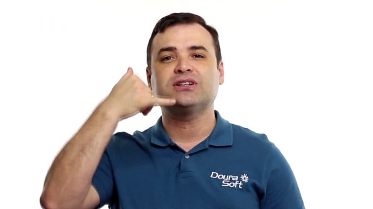 Um homem com uma camisa polo azul da Doura Soft faz um gesto com a mão imitando uma chamada telefônica, com o polegar e o mindinho estendidos perto da boca, como se estivesse perguntando: "Onde está o dinheiro?" O plano de fundo é branco.