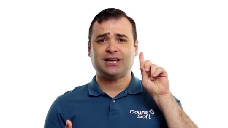 Um homem vestindo uma camisa polo azul da Doura Soft gesticula com a mão direita, erguendo o dedo indicador e olhando para frente, como se estivesse fazendo uma observação sobre a segurança dos dados. O plano de fundo é branco.
