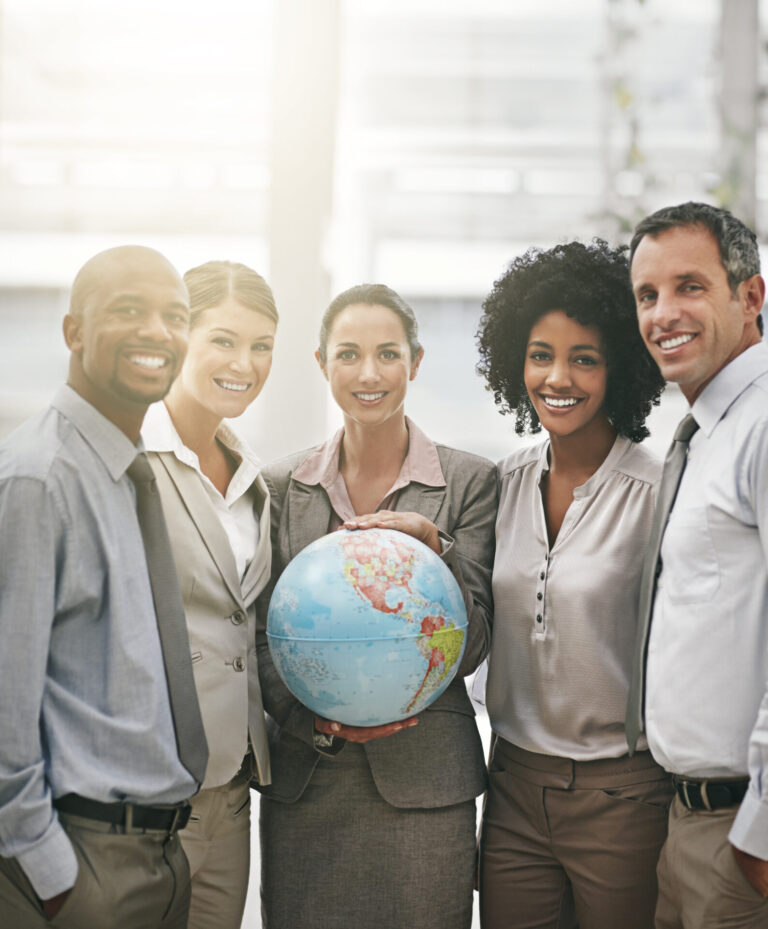 Cinco pessoas vestidas profissionalmente estão juntas, sorrindo para a câmera. A pessoa no centro segura um globo, simbolizando o trabalho em equipe global e a adaptação às mudanças, como a alteração no cronograma de implantação do esocial. O plano de fundo é claro e moderno.