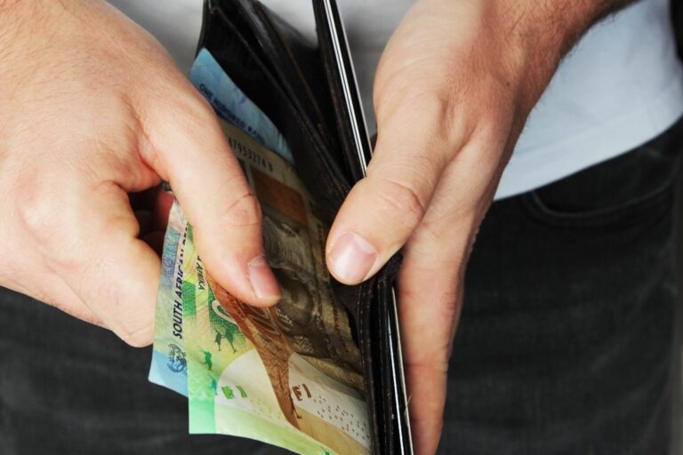 As mãos de uma pessoa segurando uma carteira aberta cheia de várias cédulas coloridas, pronta para tirar ou colocar dinheiro - uma cena cotidiana para muitos com renda per capita baixa. O fundo está fora de foco.