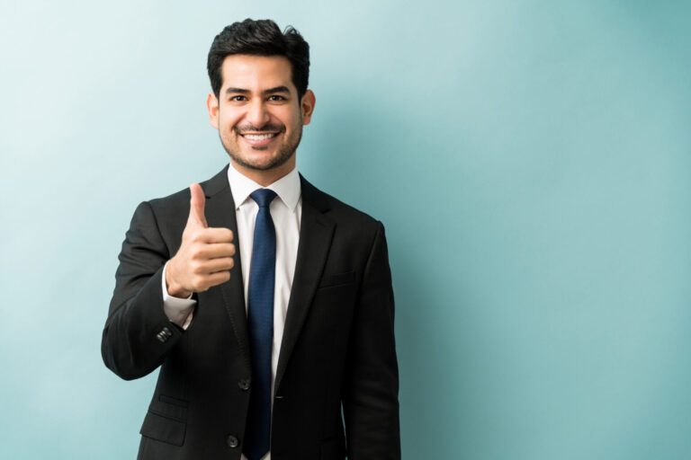 Um homem de terno preto e gravata está de pé contra um fundo azul claro, sorrindo e fazendo um gesto de polegar para cima com a mão direita, como se estivesse reagindo positivamente a uma manchete como "paulo guedes é convocado para esclarecer".