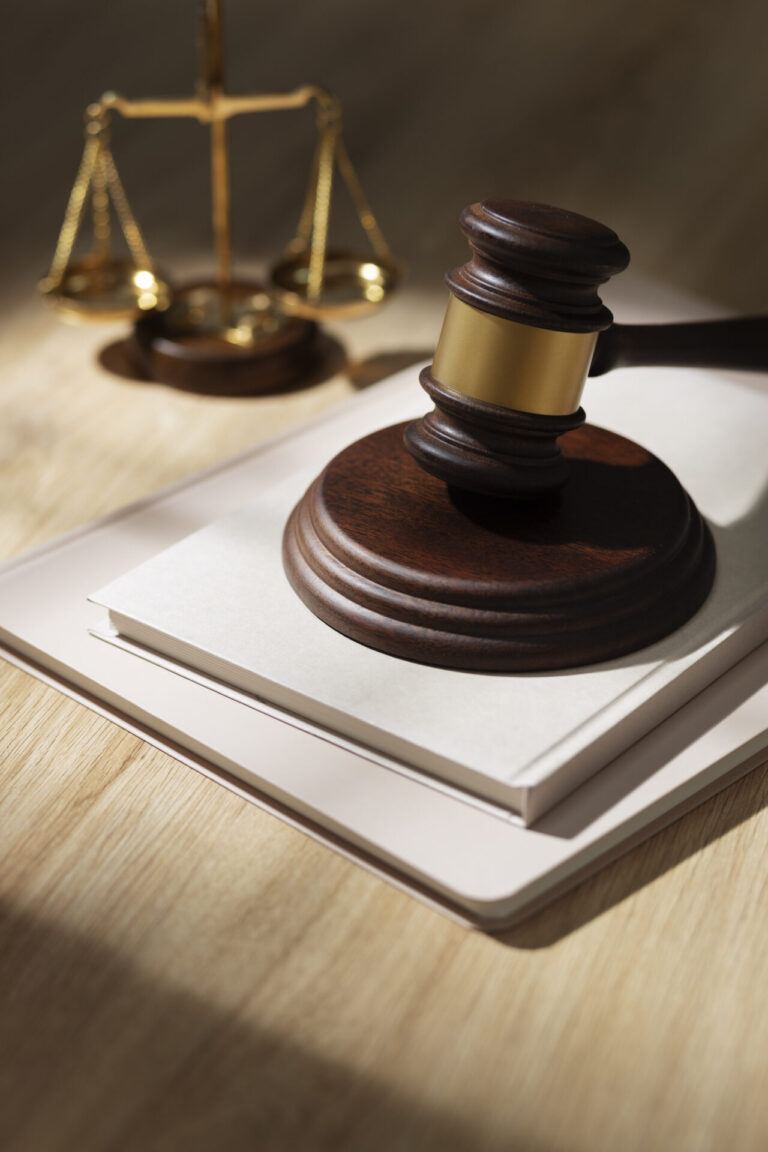 Um martelo de madeira repousa sobre um livro fechado e um laptop, com balanças douradas da justiça ao fundo, simbolizando a lei e a justiça - ecoando debates enquanto o MBL divulga vídeo em apoio à legalização.
