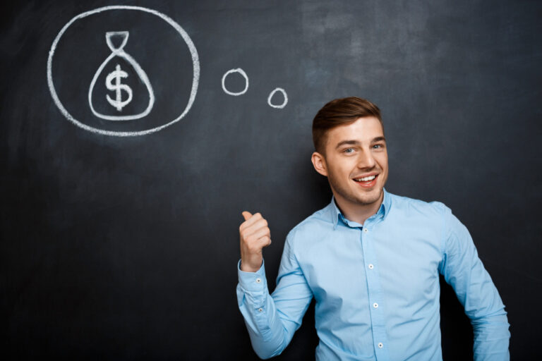 Um homem sorridente, de camisa azul clara, está em frente a um quadro negro, apontando para um desenho a giz de um balão de pensamento com uma sacola de dinheiro - simbolizando ideias para fazer aumentar a rentabilidade.