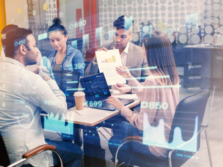 Quatro pessoas sentadas ao redor de uma mesa em um escritório discutindo um relatório comercial com gráficos, enquanto gráficos digitais destacam a gestão e a inovação, simbolizando o trabalho em equipe e a análise avançada de dados.