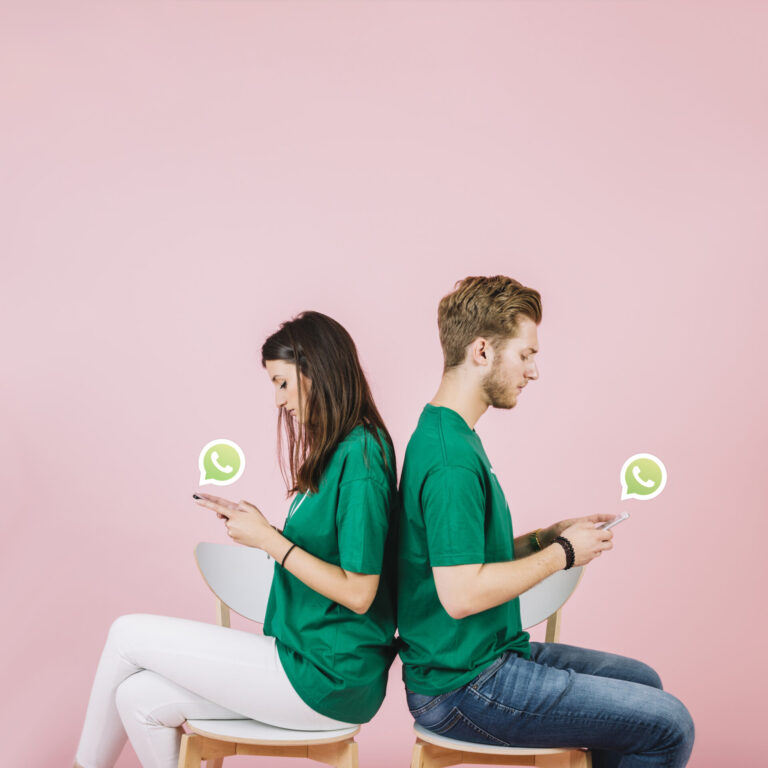 Uma mulher e um homem de camisa verde sentados de costas em cadeiras, ambos olhando para seus celulares com balões de fala do WhatsApp por perto. O fundo rosa define o cenário para o compartilhamento de 3 dicas para criar pastas do WhatsApp.