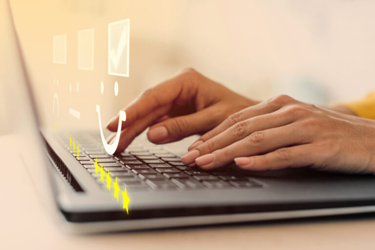Mãos digitando em um teclado de laptop com ícones digitais flutuando acima, incluindo um rosto sorridente, uma marca de verificação e cinco estrelas amarelas - sugerindo feedback on-line ou uma pesquisa de satisfação do cliente para um planner para organizar sua rotina.