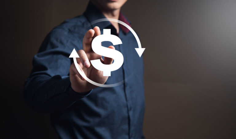 Uma pessoa de camisa azul toca um ícone de cifrão flutuante com duas setas circulares, simbolizando transações financeiras ou venda recorrente principal. O fundo é escuro e desfocado.