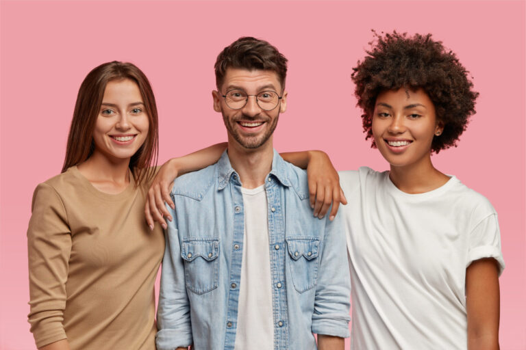 Três pessoas sorridentes estão juntas em um fundo rosa, representando os 3 tipos de unidades lotéricas. O homem no meio usa óculos e uma camisa jeans, enquanto as duas mulheres de cada lado usam camisas de cores neutras.