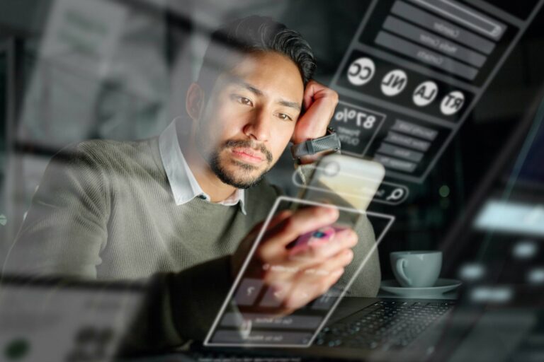 Um homem está sentado em uma mesa olhando para seu smartphone com uma expressão pensativa. Os reflexos das telas de interface digital - possivelmente de um sistema de cobrança automatizado - sugerem multitarefa ou sobrecarga digital. Um laptop e uma xícara de café estão ao fundo.
