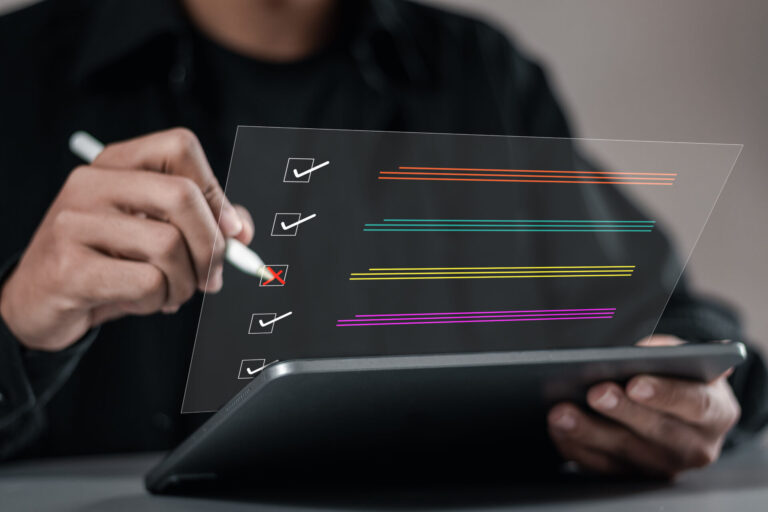 Uma pessoa usando uma caneta stylus em um tablet interage com uma lista de verificação digital, demonstrando como saber fazer uma avaliação. Quatro caixas de seleção estão marcadas, enquanto uma caixa do meio mostra um X vermelho. Linhas horizontais coloridas destacam cada item.