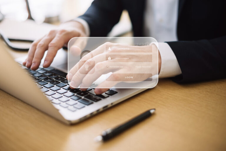 Uma pessoa de terno digita em um teclado de laptop, com uma sobreposição de formulário de login transparente mostrando nome de usuário, senha e opções de login. Um aviso sobre política de privacidade aparece; conheça as diretrizes antes de continuar. Uma caneta está sobre a mesa de madeira ao lado do laptop.